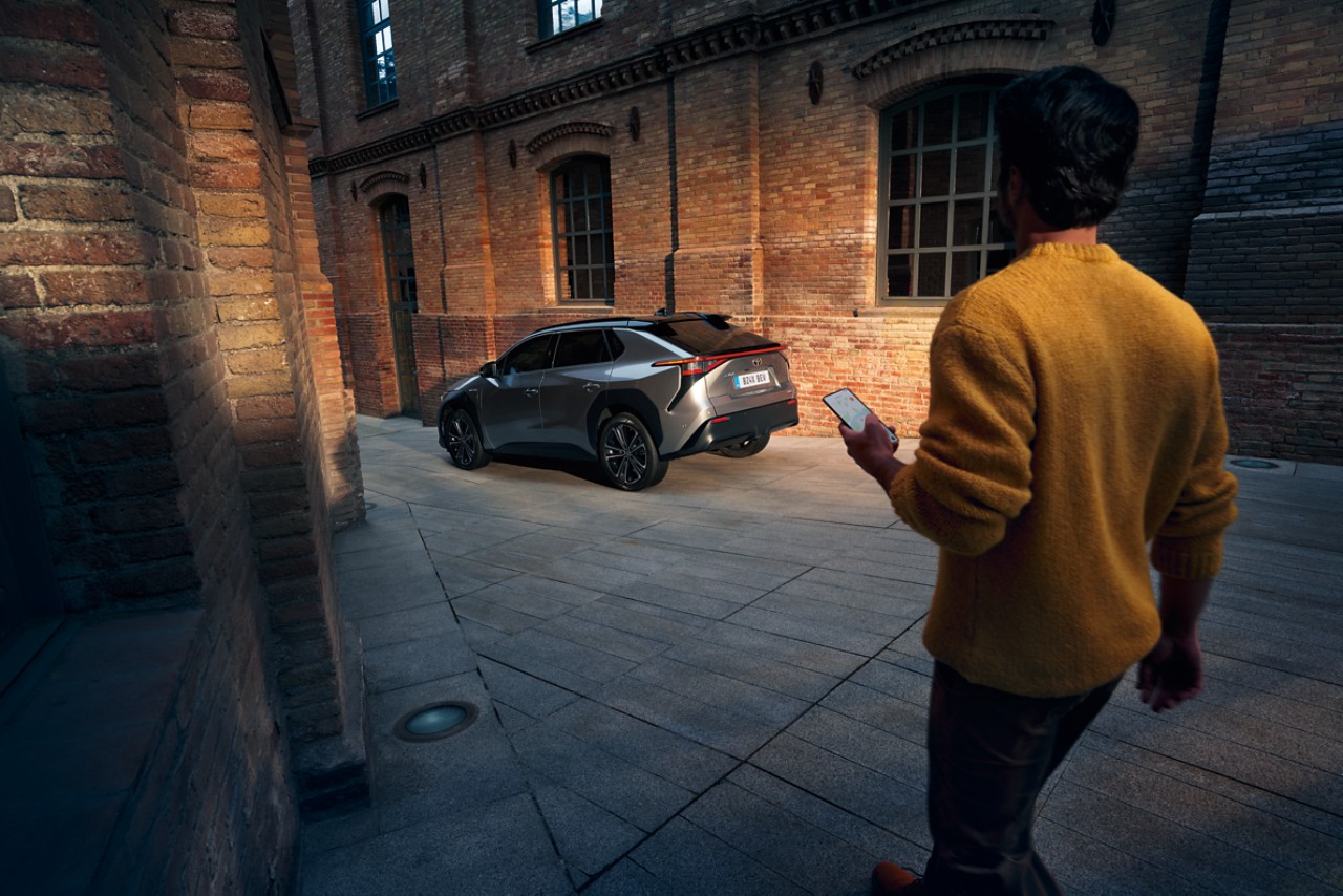 A man holding his smartphone, walking towards a car.